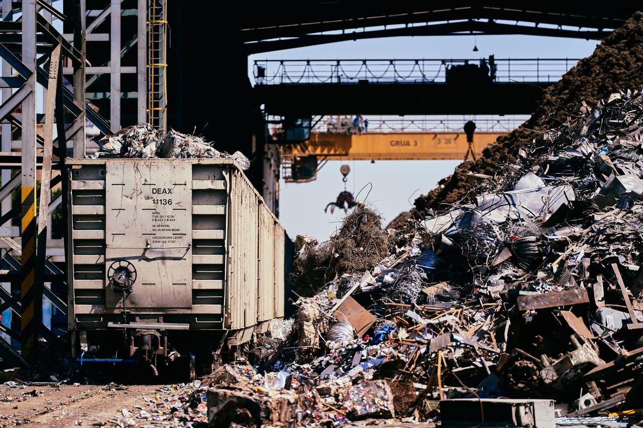 Home A dynamic industrial scene featuring a scrap yard with a train car and crane lifting debris.